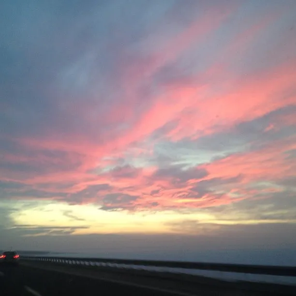 Pink and blue sunset sky over a highway with a guardrail and a car in the distance.
