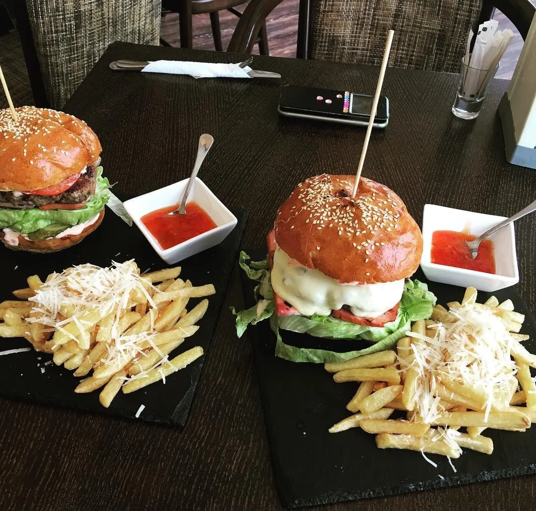 Two cheeseburgers with sesame buns, fries, and red dipping sauce served on black slate boards at a restaurant table