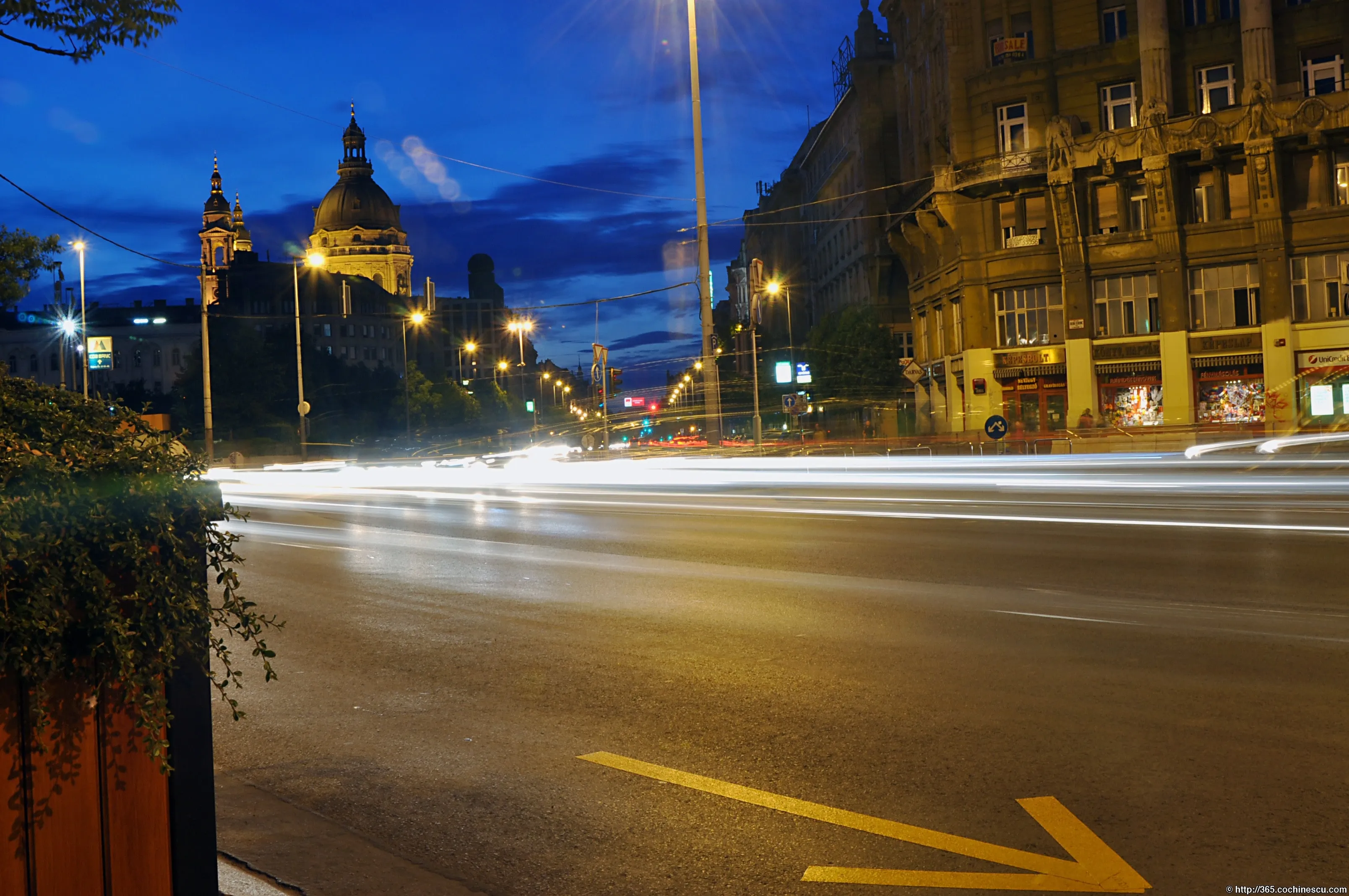 Car light trails cross a Budapest boulevard at night.