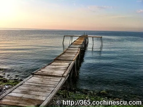 A narrow wooden pier stretches out from the shore into the calm sea.
