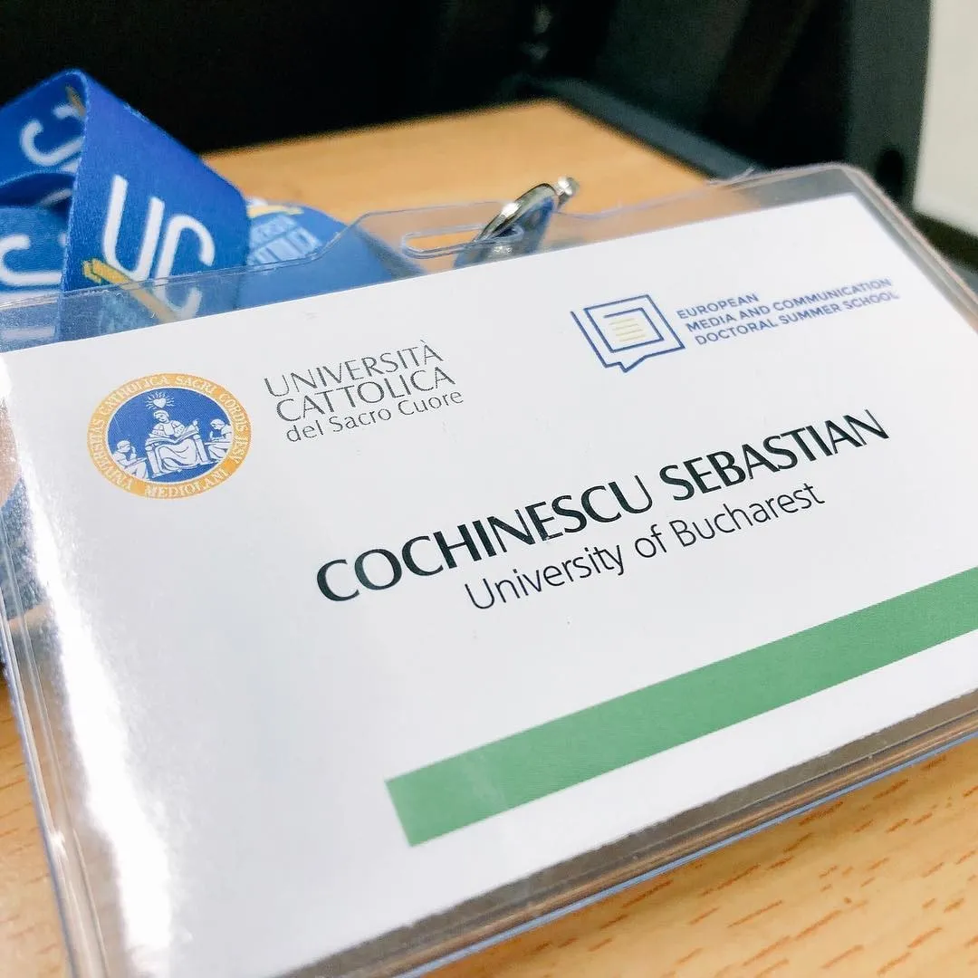 Name badge for Cochinescu Sebastian of the University of Bucharest at the European Media and Communication Doctoral Summer School, with a blue lanyard on a wooden table.