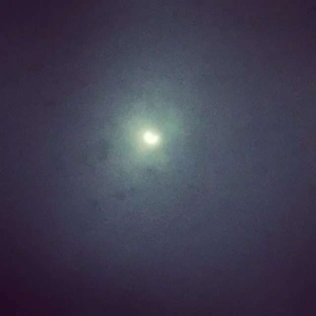 A bright glowing disk of light sits at the center of a dark, grainy sky.