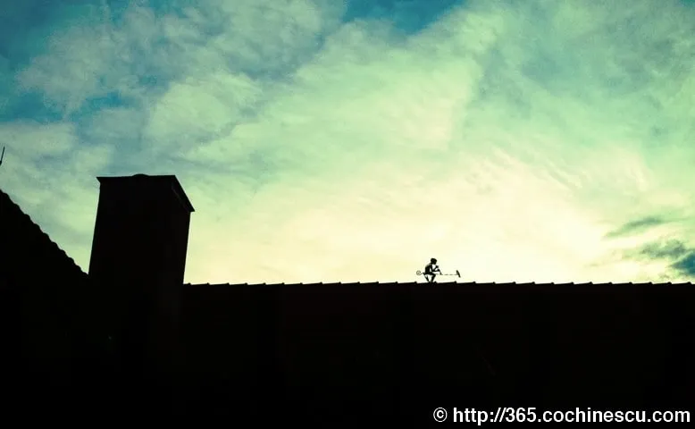 The silhouette of a chimney and a man-shaped weather vane can be seen on the roof against the sky.