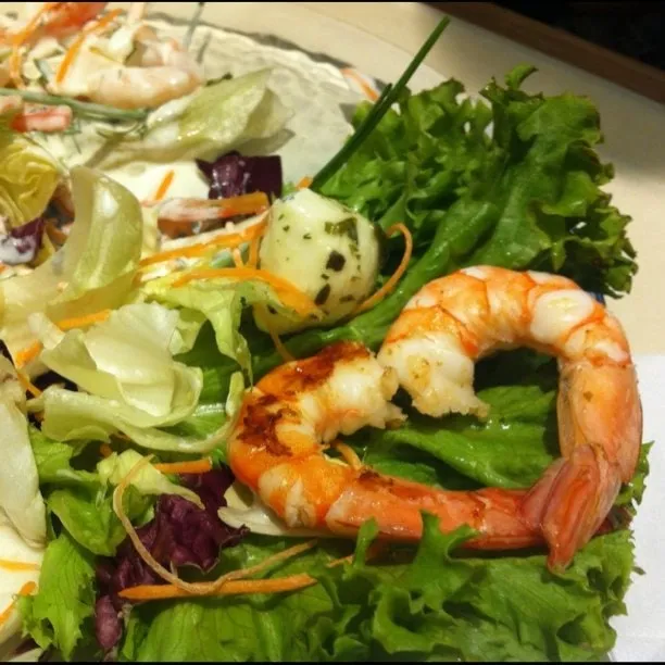 Cooked shrimp arranged in the shape of a heart on a green leaf salad, with carrot strips and a marinated clam.