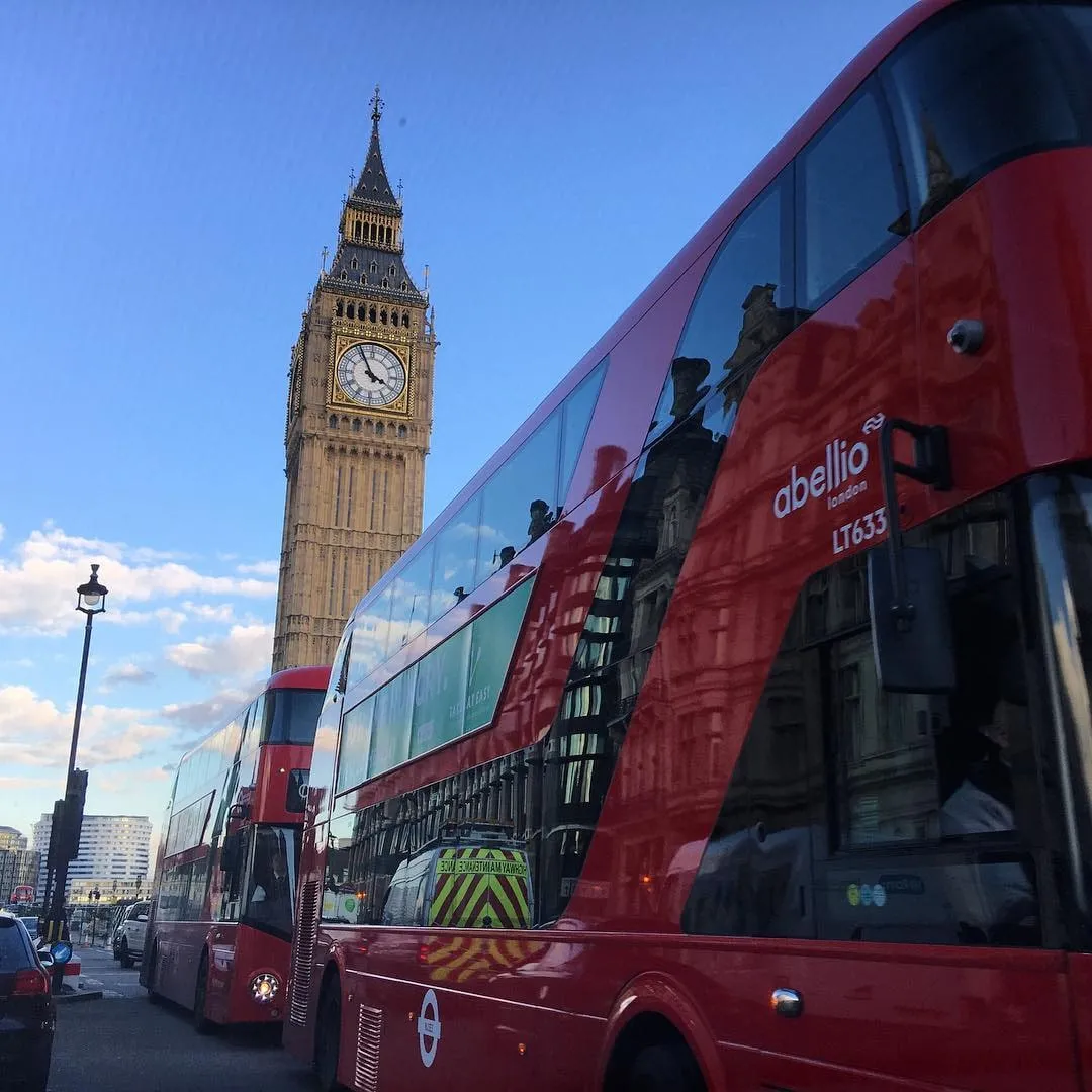 Red double-decker buses on a London street with Big Ben rising behind them against a blue sky.