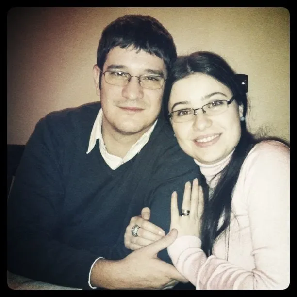 Cătălina and Sebastian, a couple wearing glasses, smile in a close-up portrait.