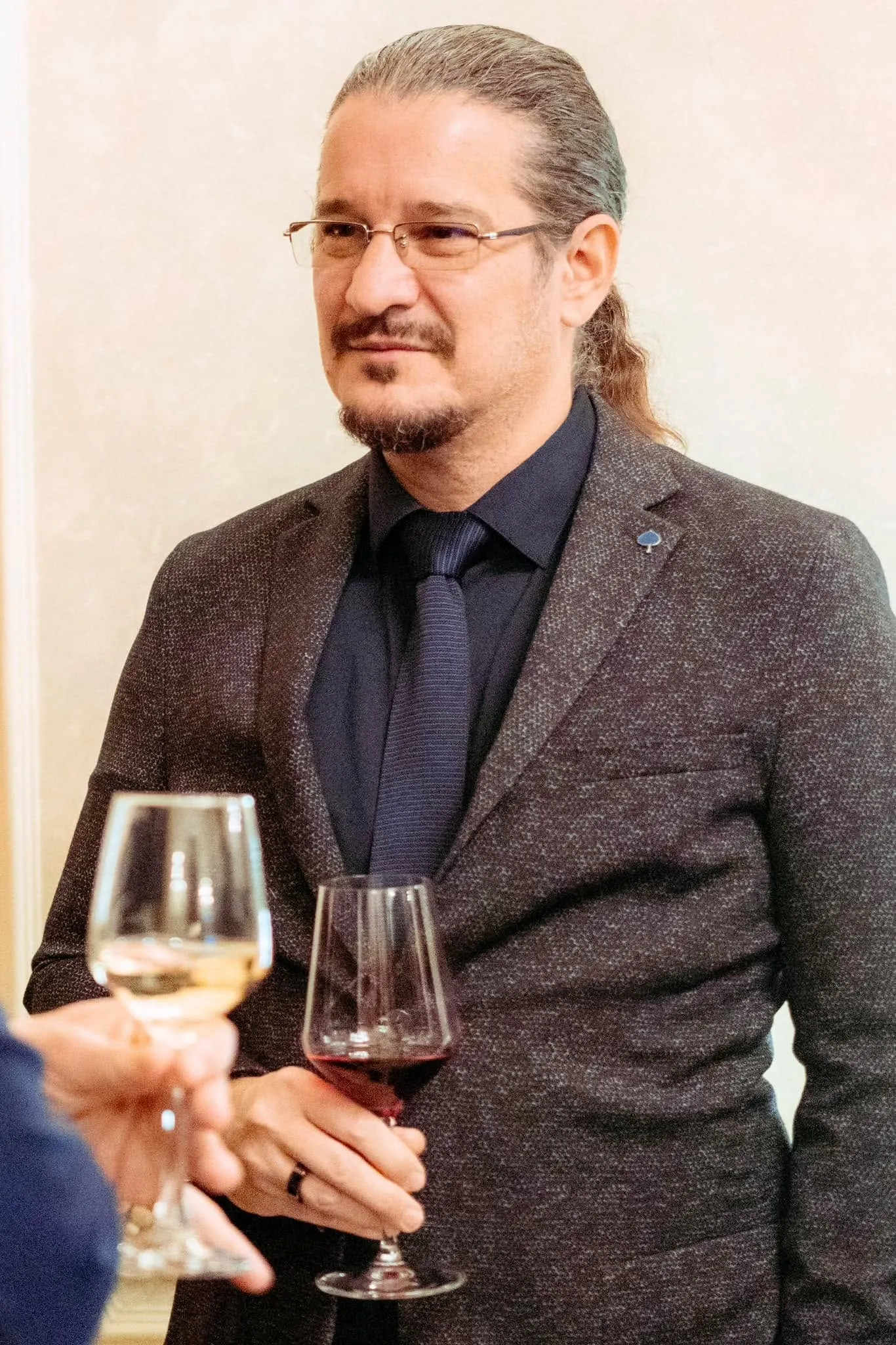 Sebastian Cochinescu stands in formal attire at a reception while holding a glass of red wine.