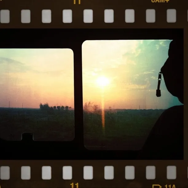 Sunset seen through the train window, with the silhouette of a passenger against a backdrop of fields.