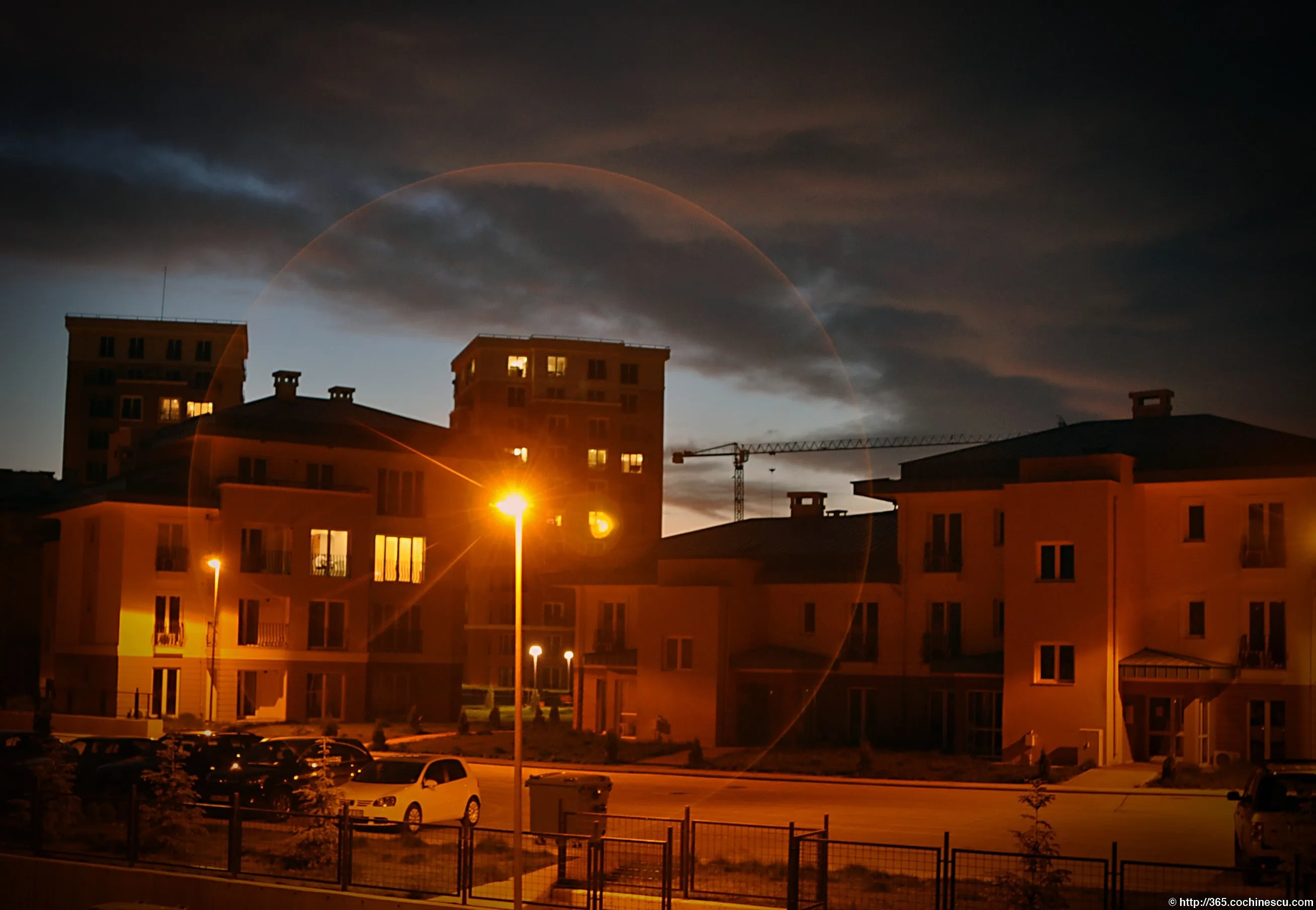 The apartment buildings and houses in a neighborhood are lit up at night beneath a cloudy sky.