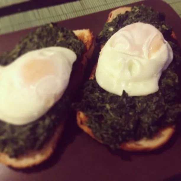 Two slices of toast topped with spinach and sunny-side-up eggs on a plate