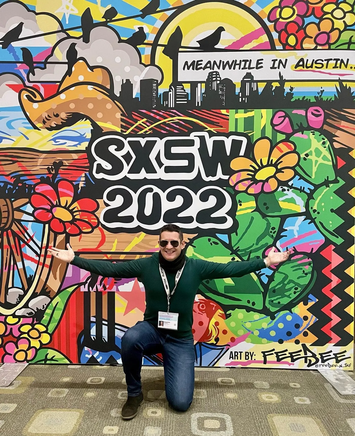 Sebastian Cochinescu poses with open arms in front of a colorful SXSW 2022 mural.