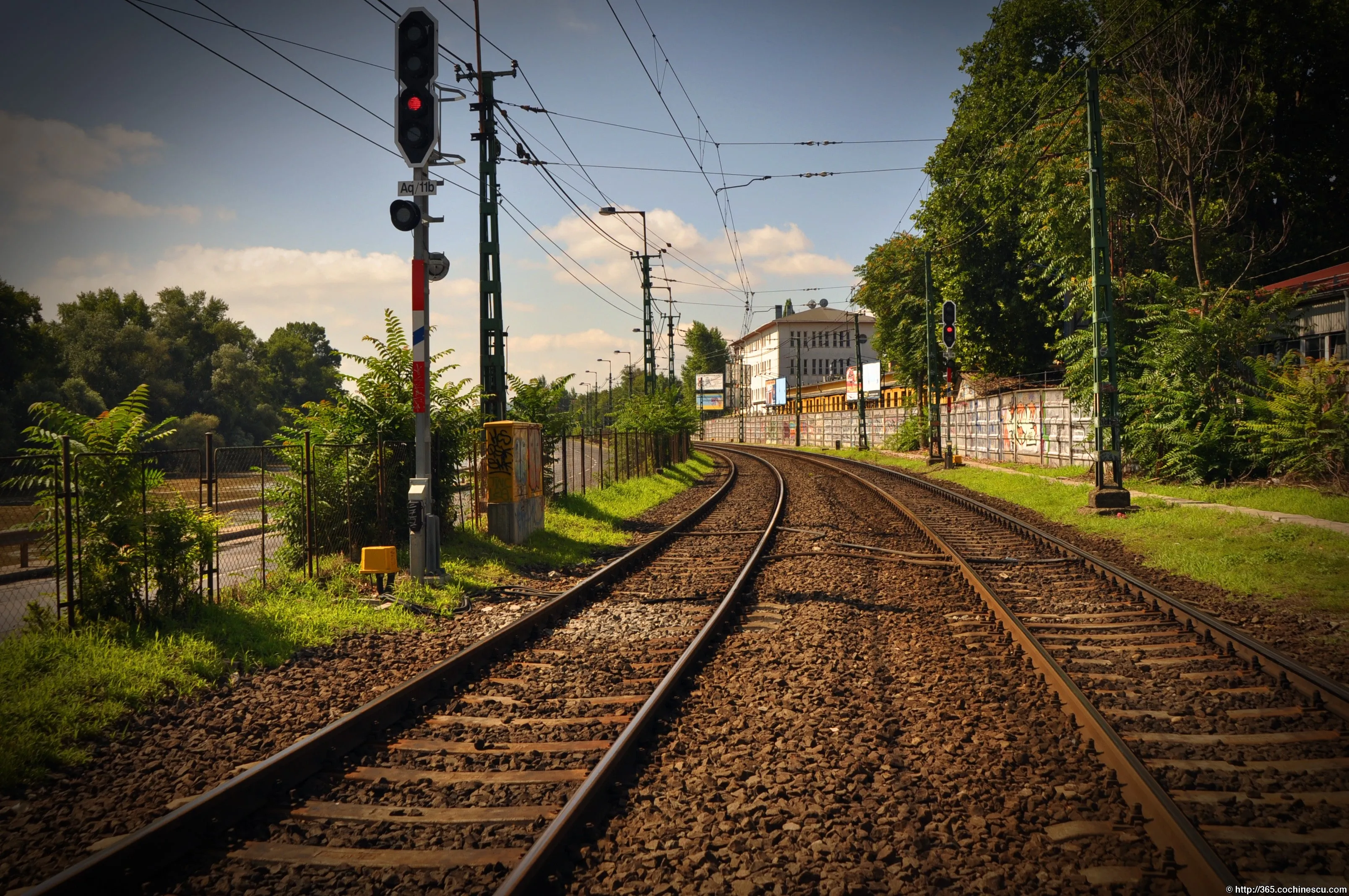 Two electrified railway tracks curve among trees and buildings.