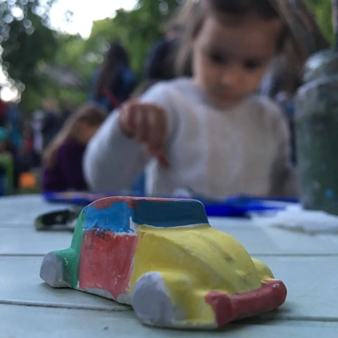 A colorful hand-painted clay toy car on a table with a child painting in the blurred background