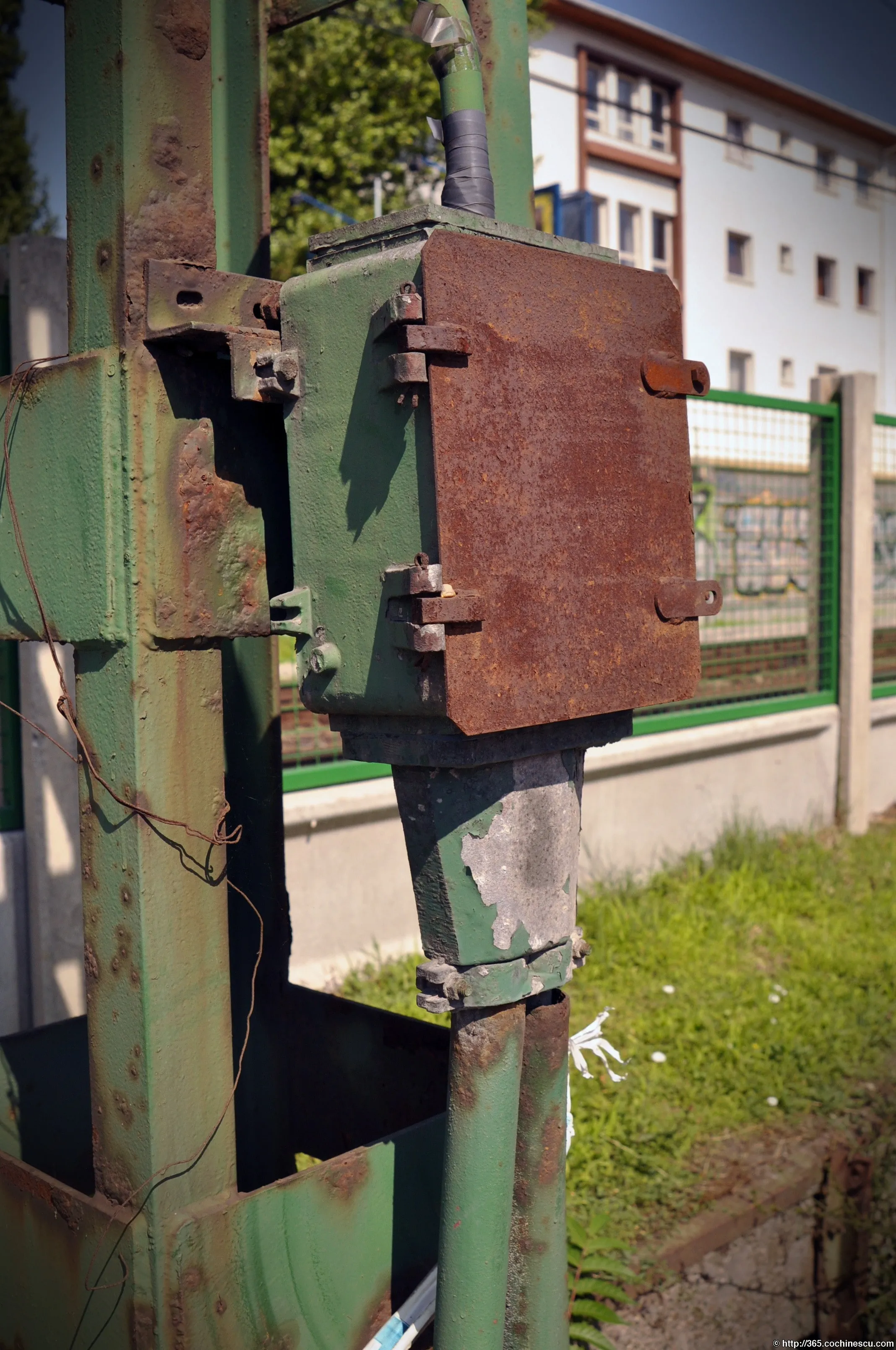 A rusty electrical mechanism mounted on a green metal pole in Budapest.