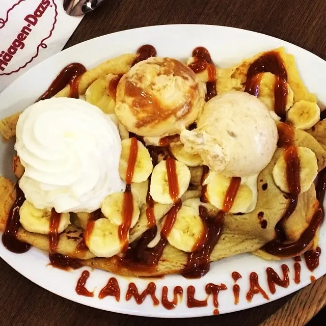 A plate of pancakes, bananas, ice cream and whipped cream, with HAPPY BIRTHDAY written in sauce around the edge.