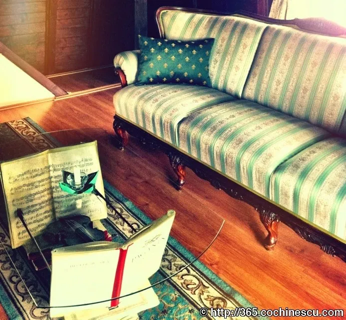 A violin, a bow and some sheet music are lying on the floor next to a sofa.