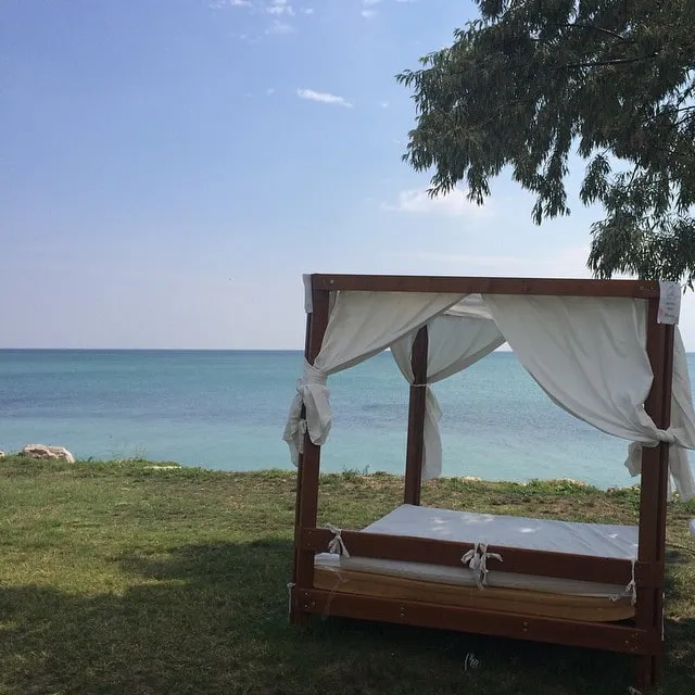 Wooden four-poster bed with white curtains by the turquoise sea.