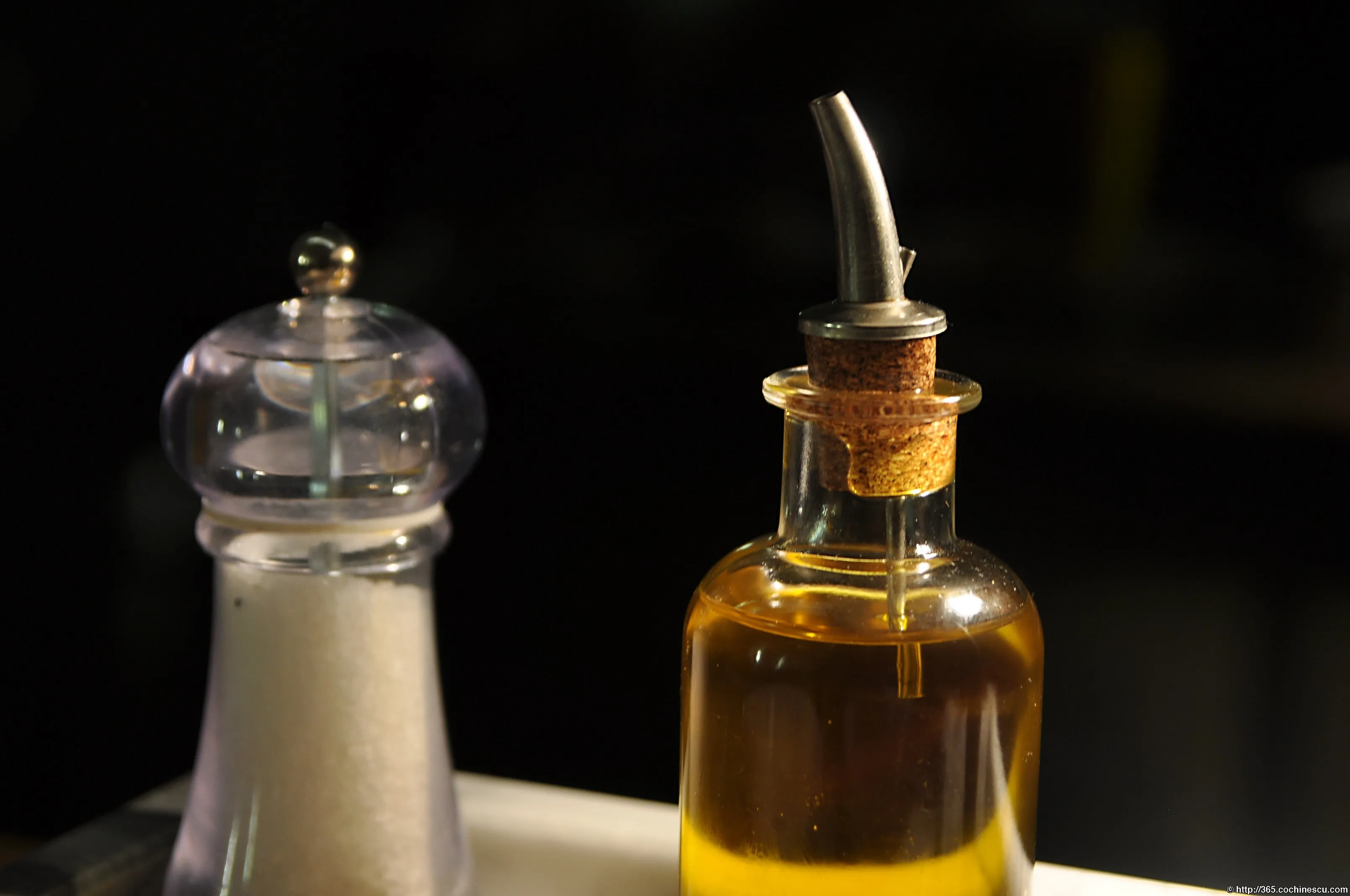 A salt grinder and a bottle of oil sit on a table.