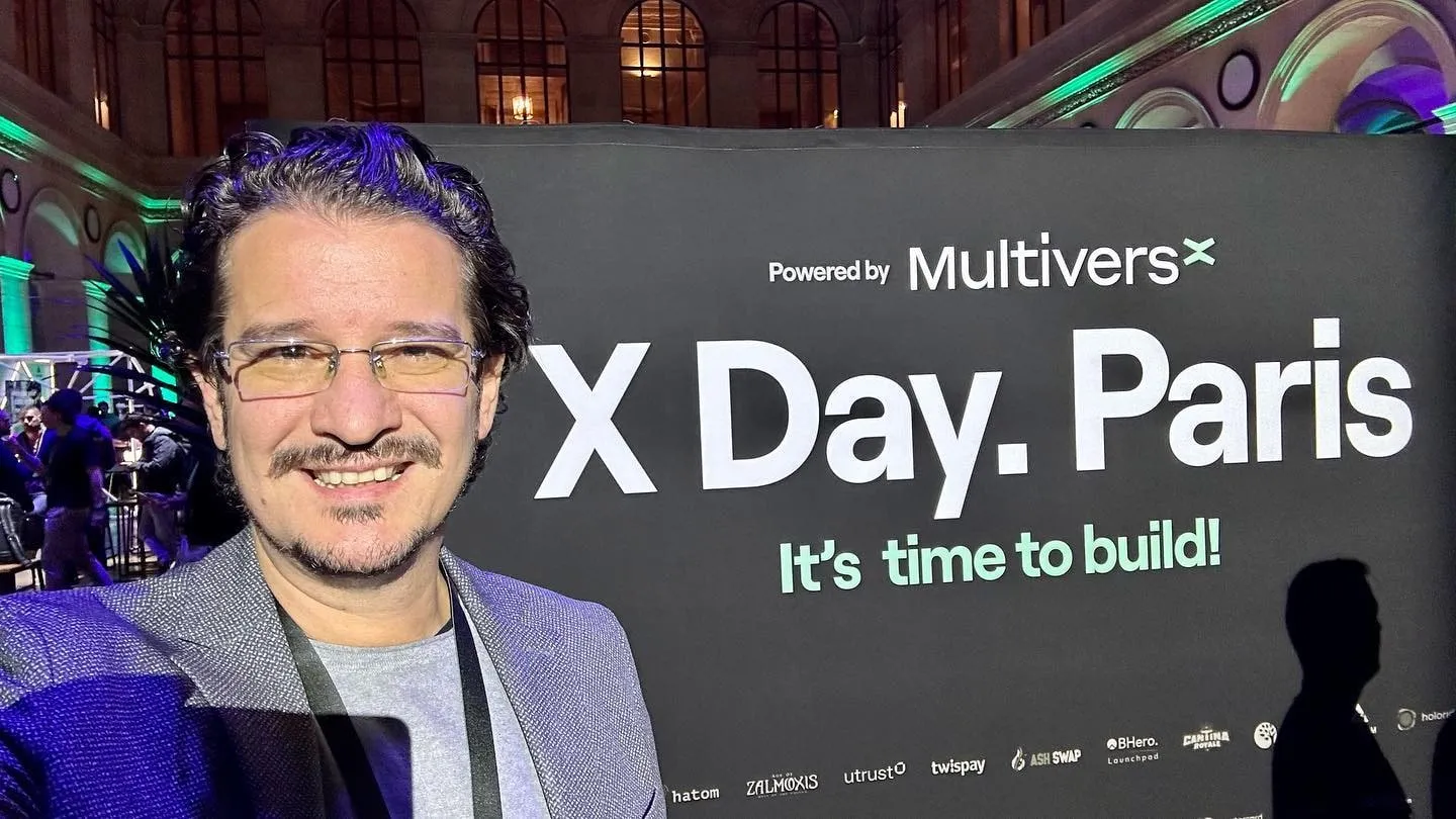 Man in glasses smiling in a selfie beside an X Day Paris banner powered by MultiversX.