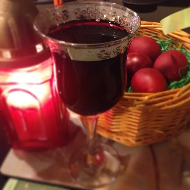Glass of red wine, basket of red Easter eggs, and a lit candle on the table