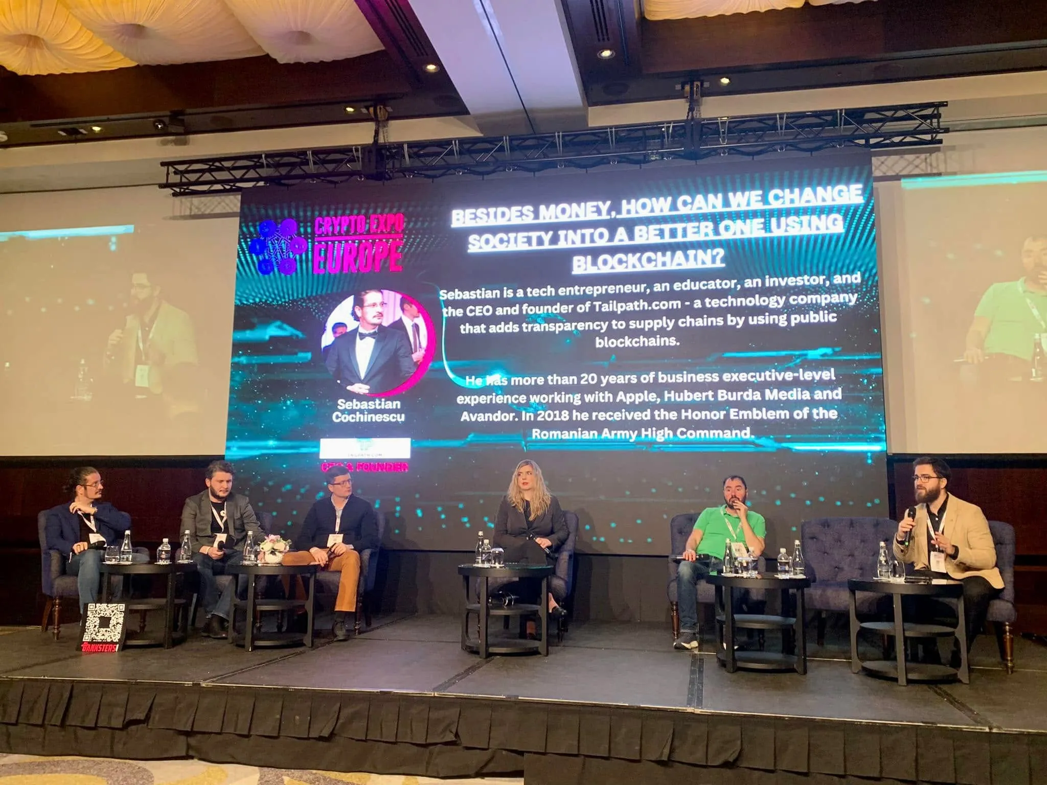 Six panelists sit on stage at Crypto Expo Europe beneath a large screen showing Sebastian Cochinescu’s speaker bio.