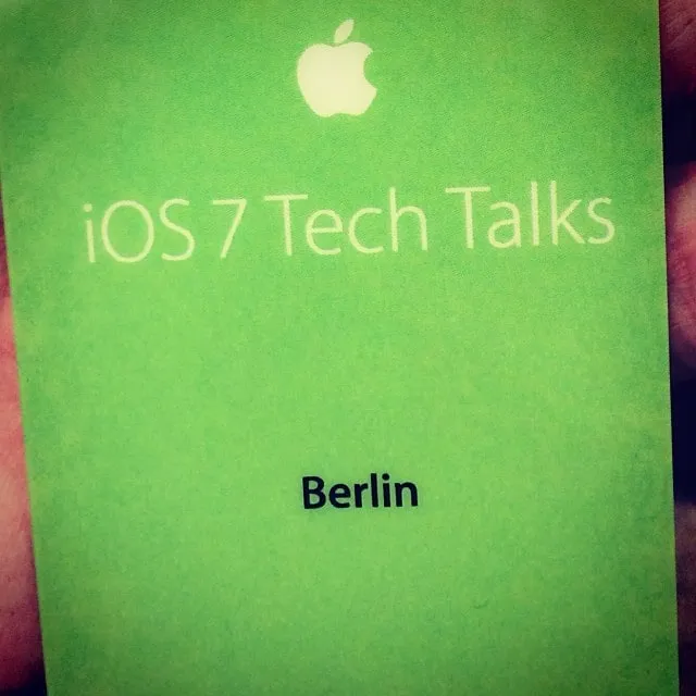 A green Apple badge labeled iOS 7 Tech Talks Berlin is held between fingers.