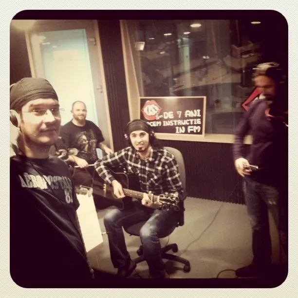 The members of Hara with guitars in a Kiss FM radio studio, next to a blue logo sign
