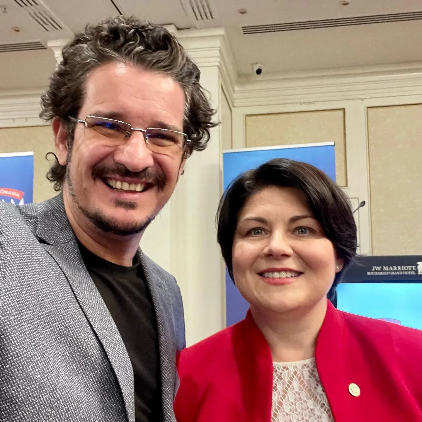 Man in a gray blazer and Natalia Gavrilița in a red jacket pose together at an indoor event.