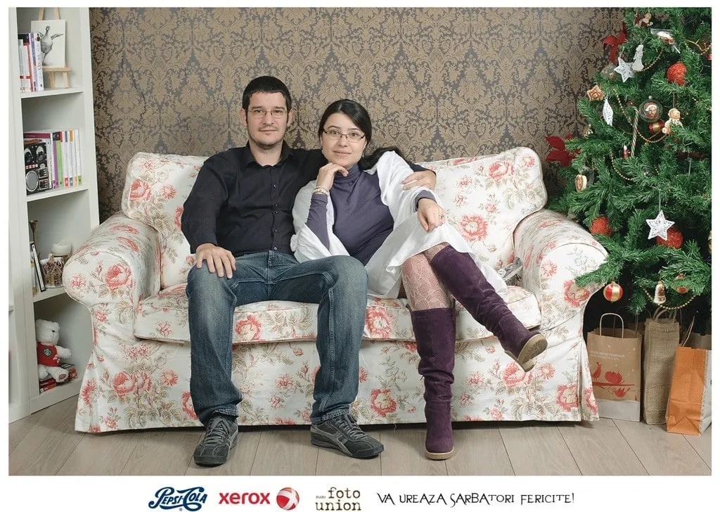 Cătălina and Sebastian sitting together on a couch next to the Christmas tree.