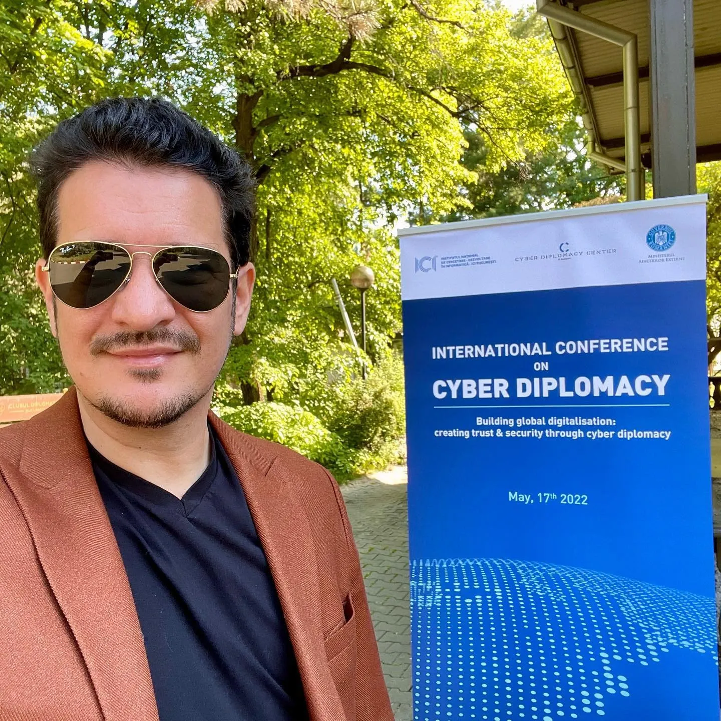 Sebastian Cochinescu stands beside a Cyber Diplomacy Conference banner outdoors.