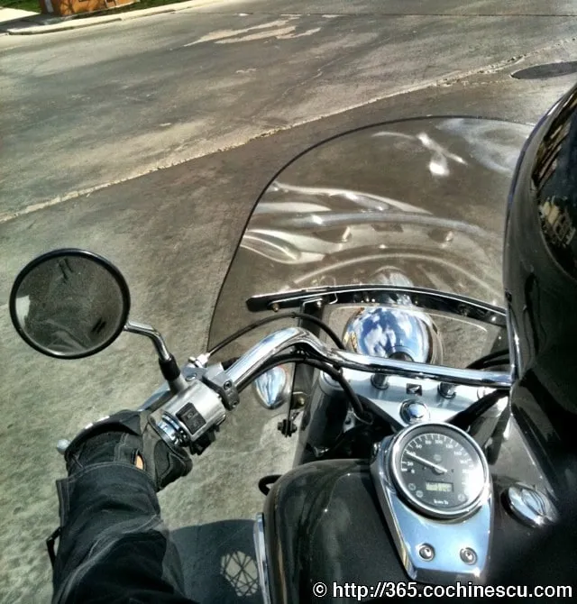 Motociclistul privește peste ghidonul și parbrizul unei motociclete oprită pe stradă.