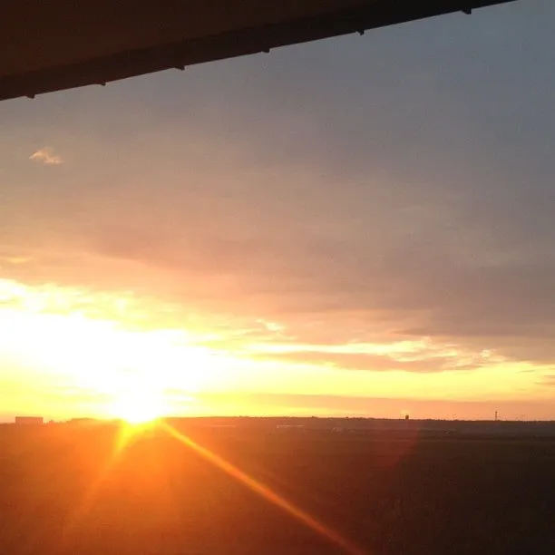 A brilliant sunrise over an open field, seen from under a roof.
