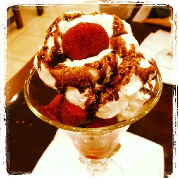 Glass sundae topped with whipped cream, chocolate sauce, and a whole strawberry.