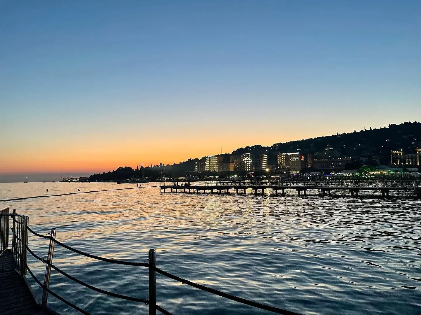 The sun sets over the waterfront, piers, and illuminated hotels in Portorož.
