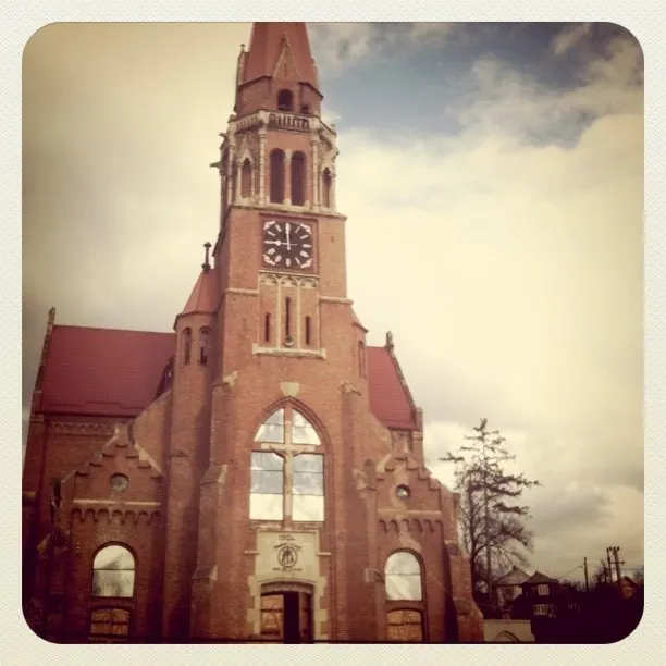 Red-brick cathedral with a Gothic tower and clock, photographed from below against a cloudy sky
