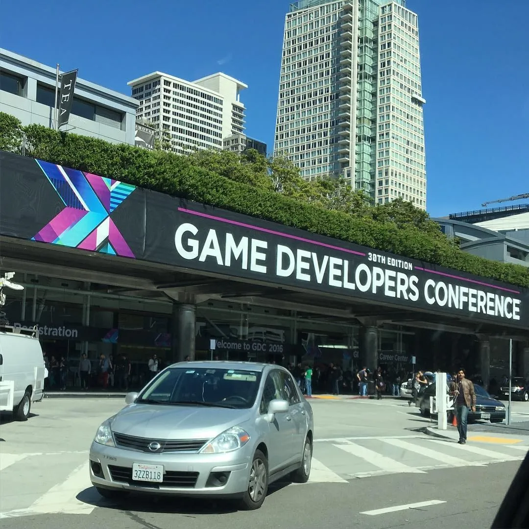 Entrance banner for the Game Developers Conference 30th Edition with a silver car and city high-rises behind it