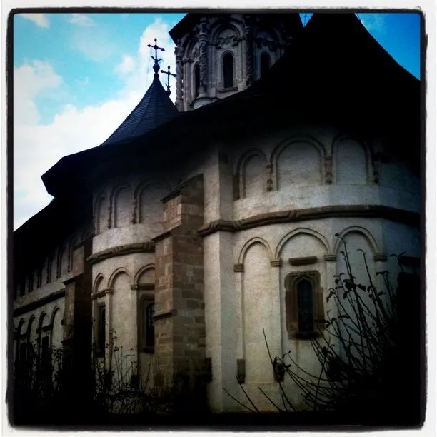 The stone building of Putna Monastery, with towers and crosses against a cloudy sky.