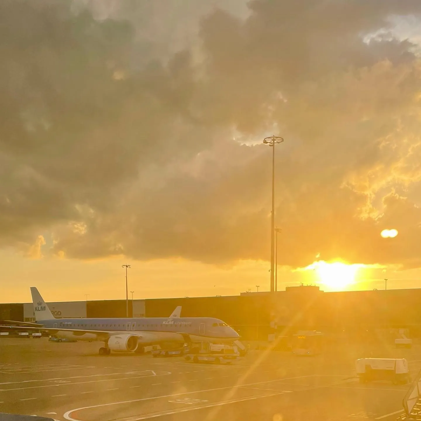 Golden sunlight breaks through heavy clouds above an airplane parked at an airport.