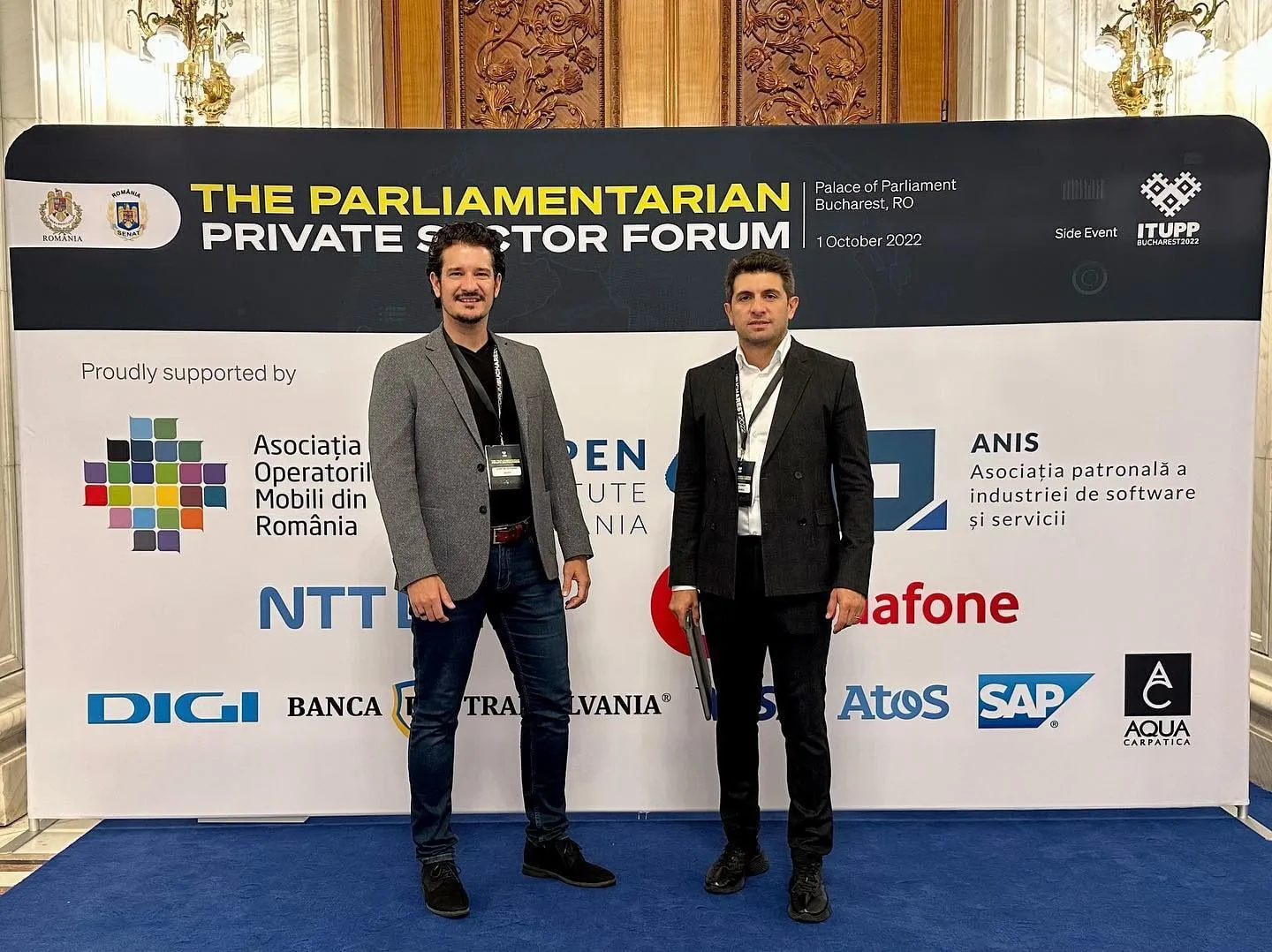 Two men pose in front of the Parliamentarian Private Sector Forum backdrop at the Palace of Parliament.