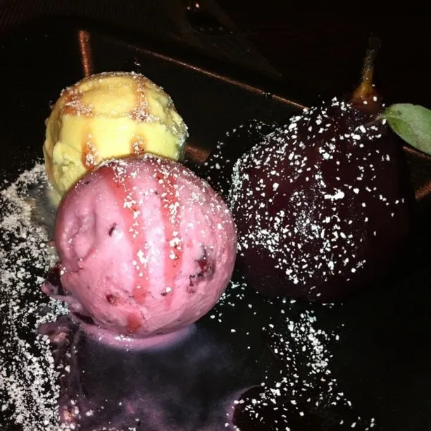 Wine-poached pear with two scoops of ice cream on a black plate, dusted with powdered sugar.