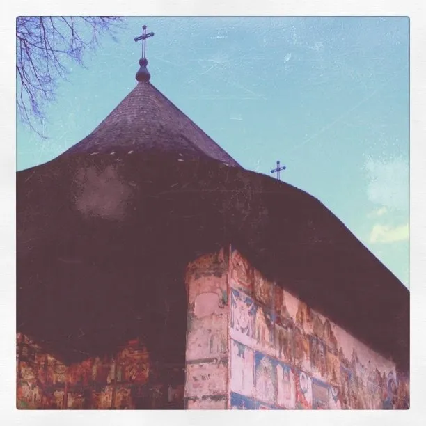 Conical roof with crosses and exterior frescoes on the walls of Arbore Church.