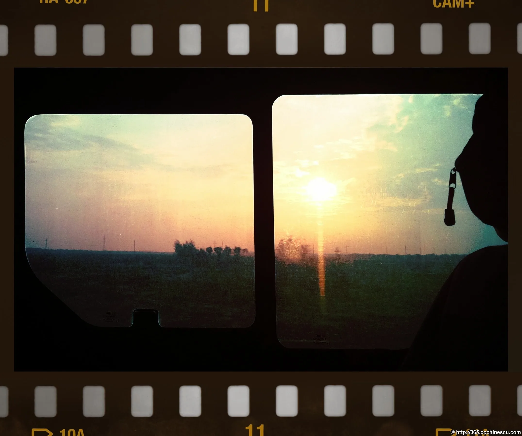The sun setting over a field, seen through a coach window.