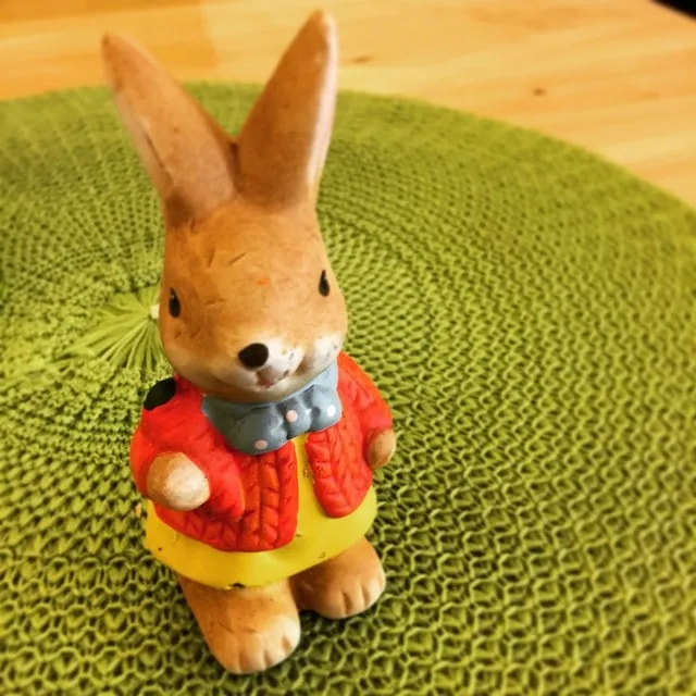 Small ceramic bunny figurine in a red cardigan and yellow skirt on a green woven placemat