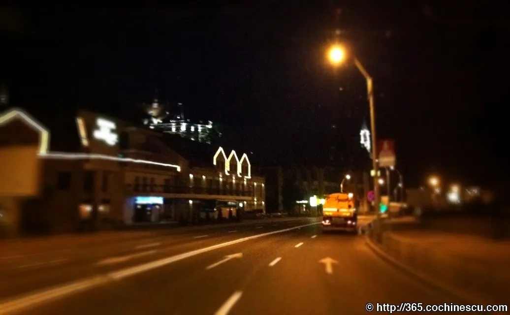 A street lit up at night, seen from a moving car.