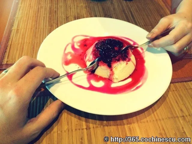 Two people sharing a dessert with red sauce and berries.