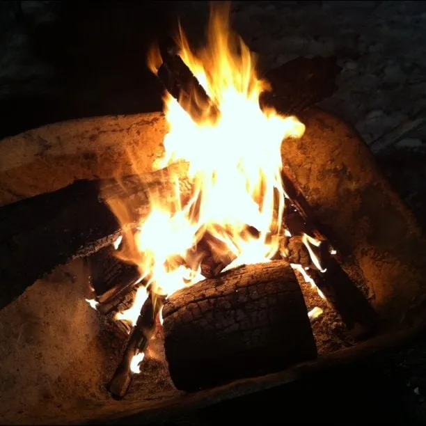 A wood fire burns in a metal wheelbarrow on the snow at night.
