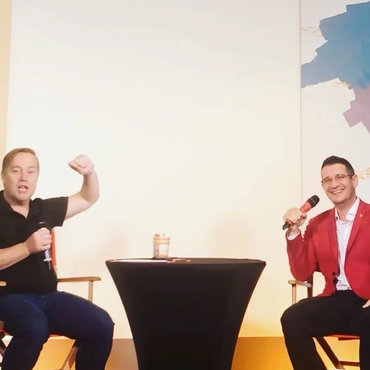Jason Calacanis and Sebastian Cochinescu sit onstage holding microphones during a conversation.