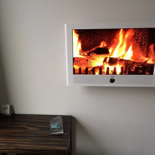 White wall-mounted TV displaying a fireplace, above a dark wooden table