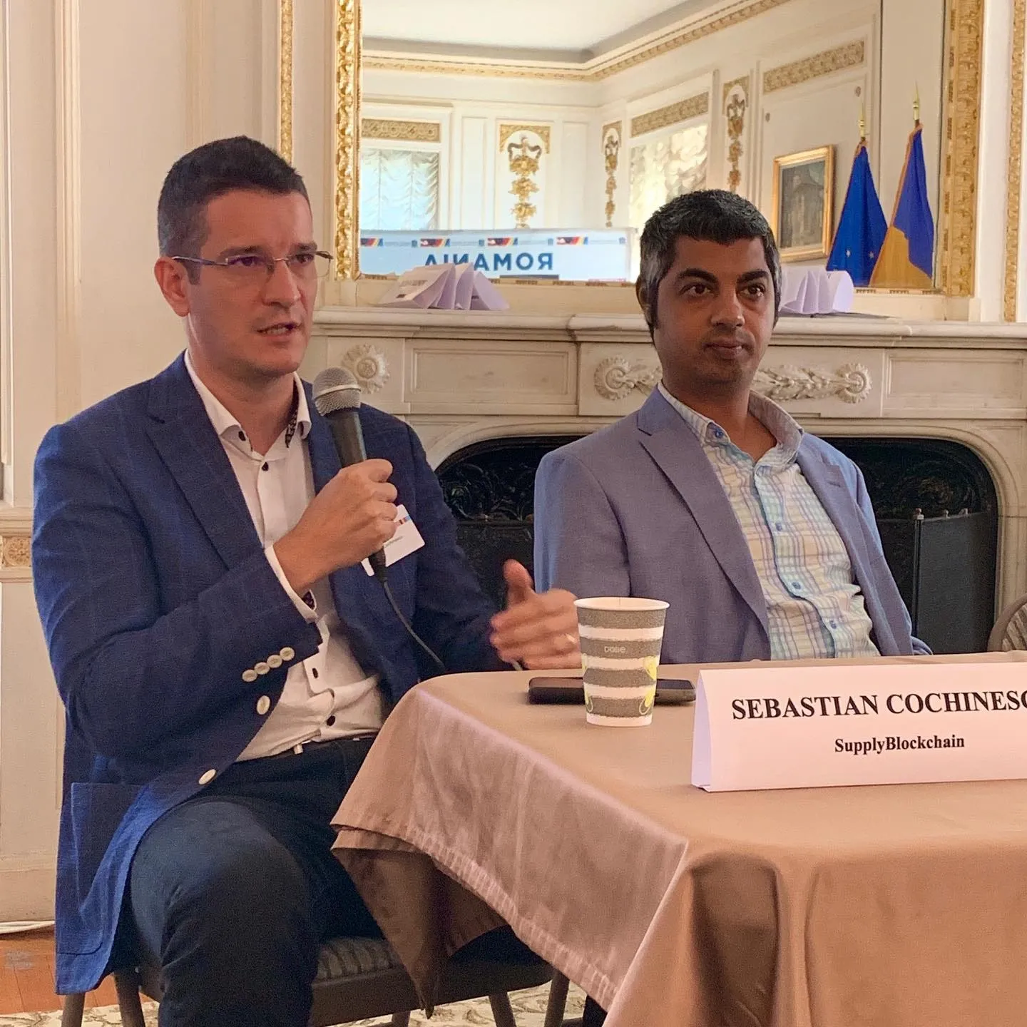 Sebastian Cochinescu speaks into a microphone beside another panelist at the Romanian Embassy in Washington, DC.