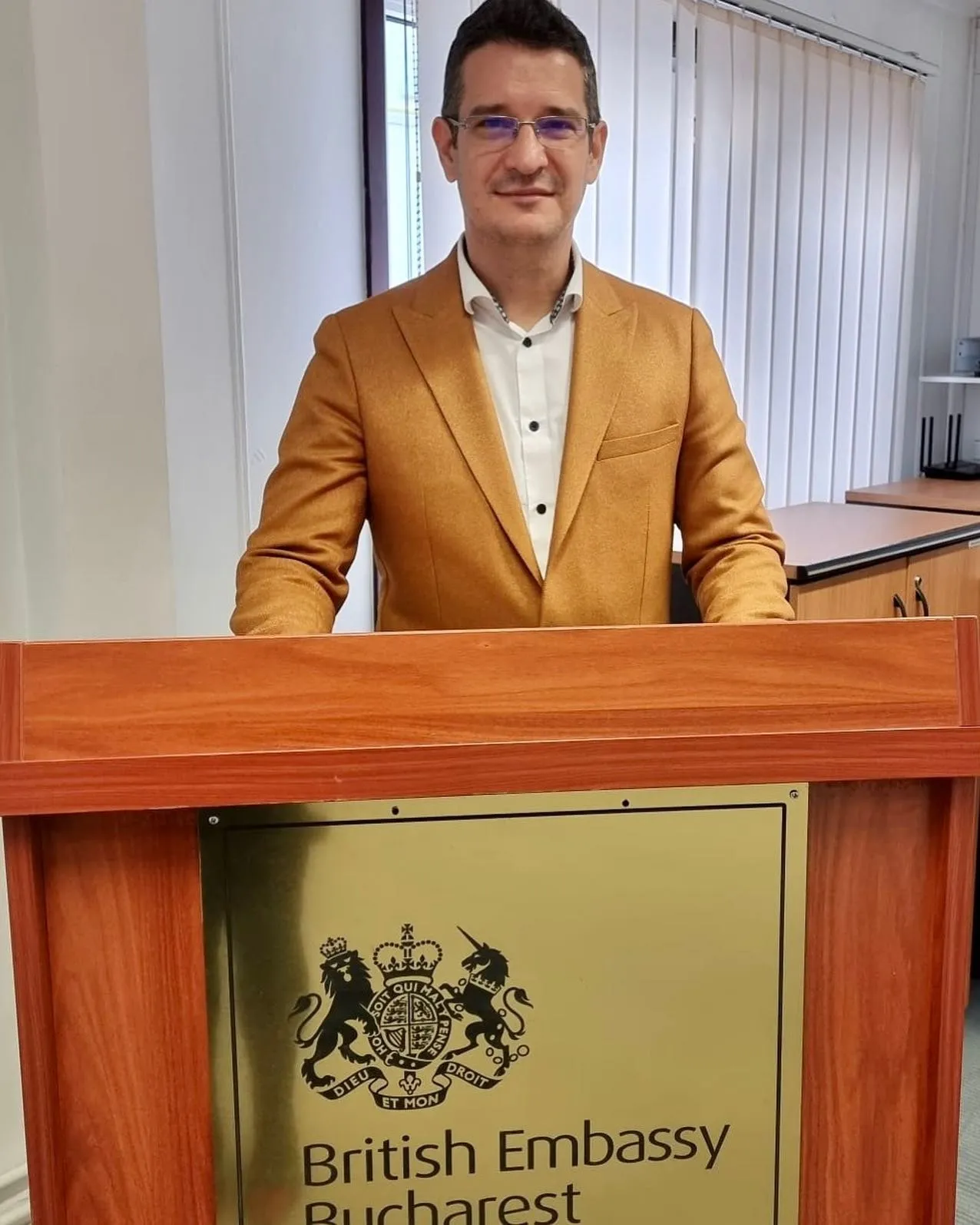 Sebastian Cochinescu stands behind a lectern bearing the British Embassy Bucharest crest.